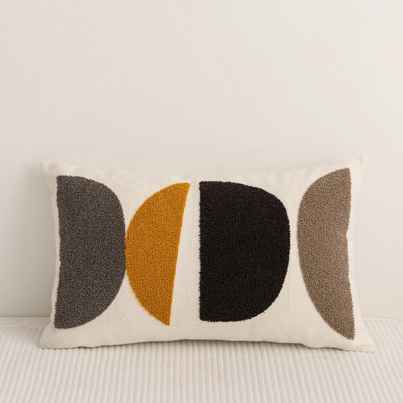 Coussin de style minimaliste avec formes géométriques en différentes couleurs neutres, posé sur un sol en bois.