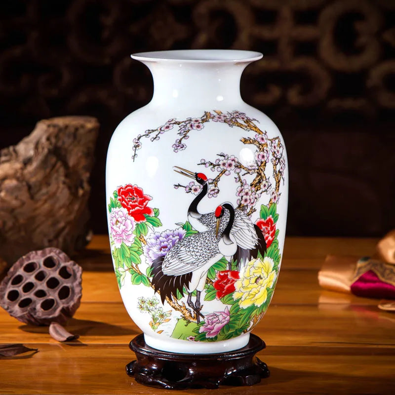 Sur un support en bois, un vase en porcelaine blanche est orné de motifs floraux et de grues peints à la main avec des couleurs vives.