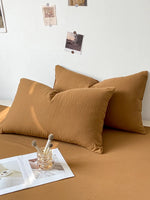 Cette image montre un décor de chambre à coucher confortable, avec deux oreillers marron sur un lit, des photos accrochées au mur et des objets décoratifs posés sur une surface.