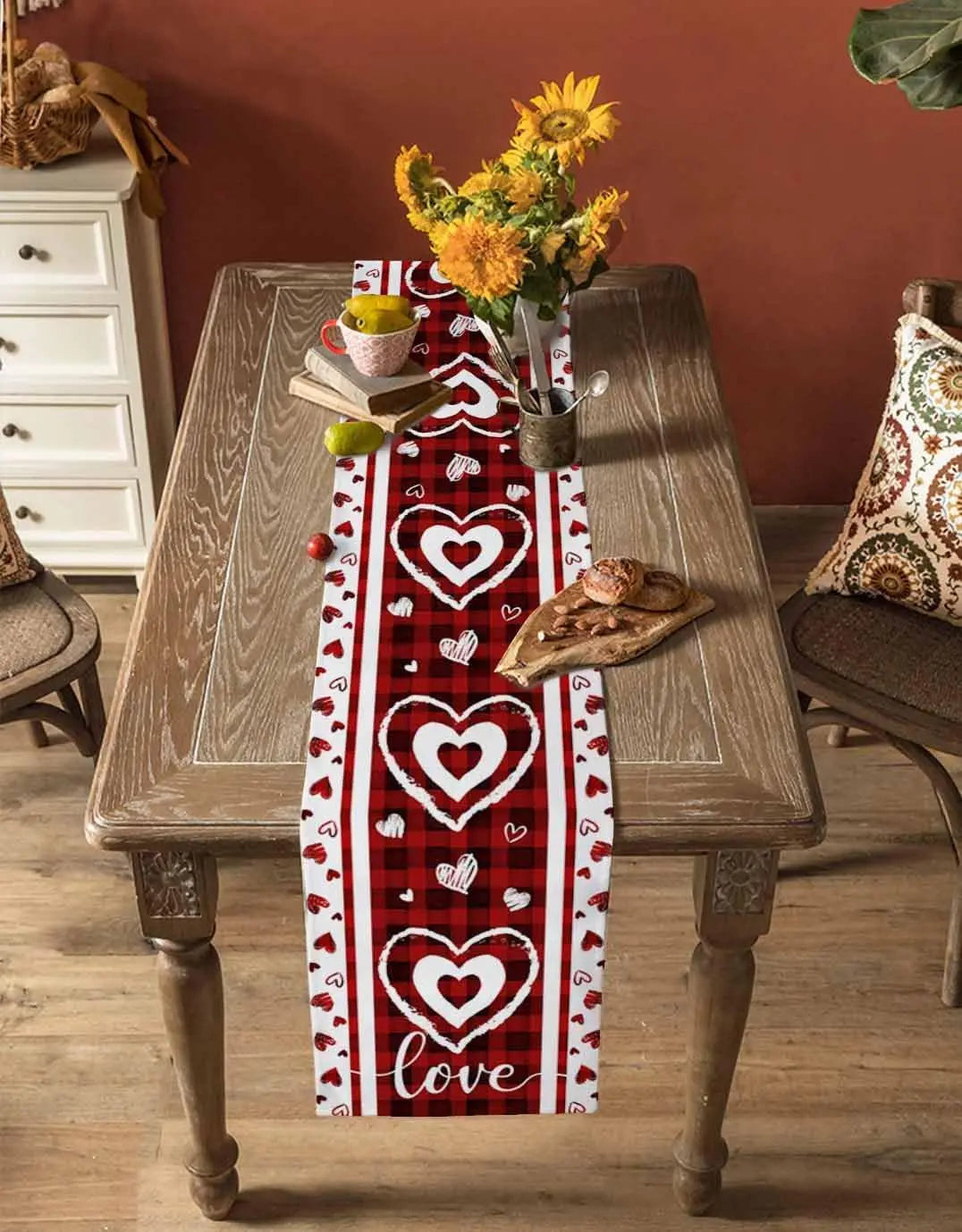Une table en bois rustique avec un chemin de table en motif cœur rouge et blanc, une bouquet de fleurs jaunes, et des pommes vertes posées sur la table.