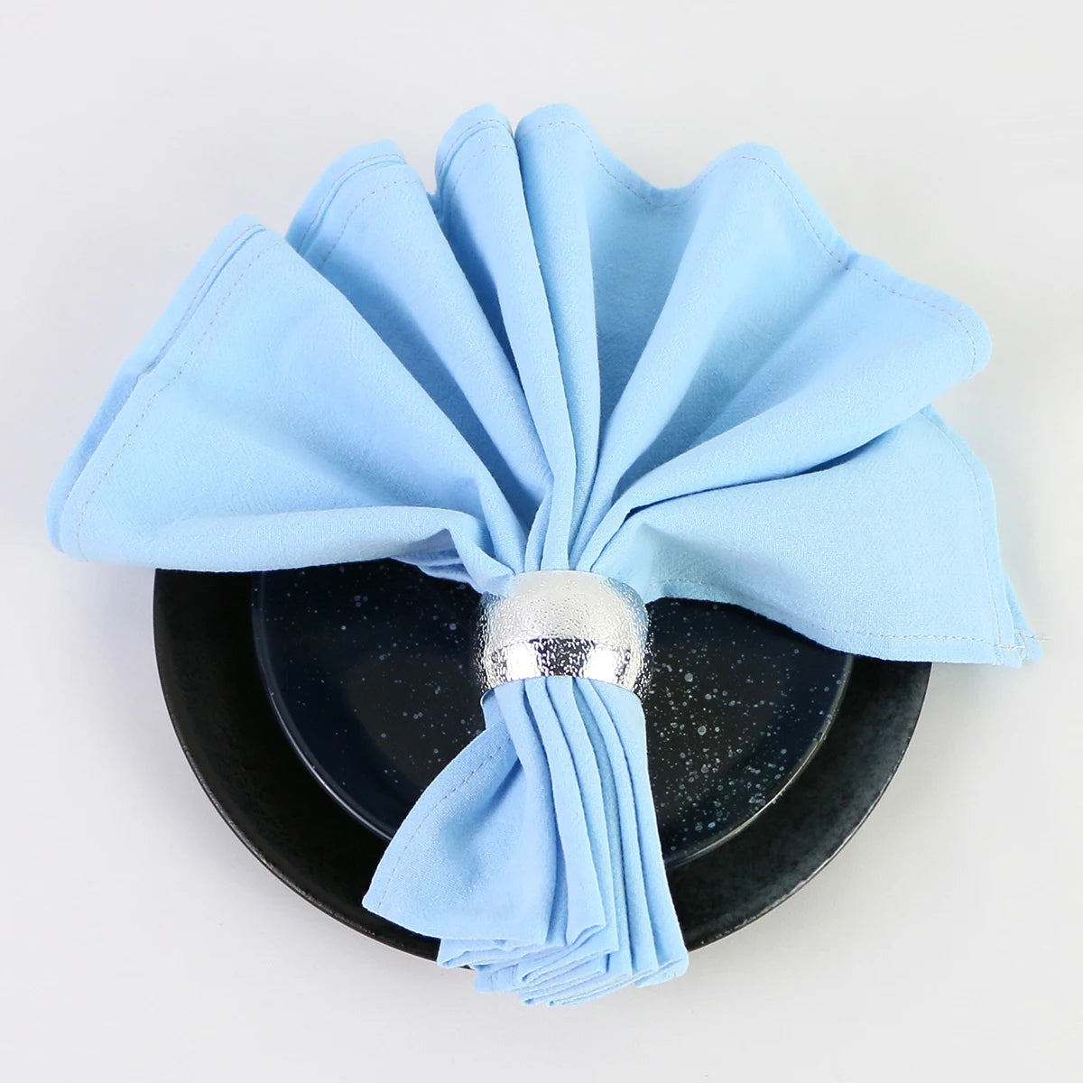 Une serviette en microfibre bleue ciel artistiquement pliée sur une assiette noire avec des paillettes, créant une belle composition élégante.