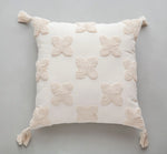 Coussin décoratif blanc en forme de fleurs avec pompons aux coins.