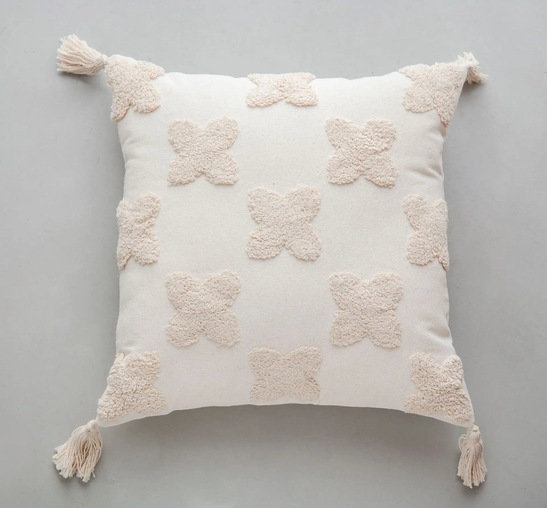 Coussin décoratif blanc en forme de fleurs avec pompons aux coins.