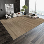 Un salon moderne avec un canapé et des coussins beiges, une grande fenêtre avec vue sur la nature, et un tapis beige qui couvre le sol en bois foncé.