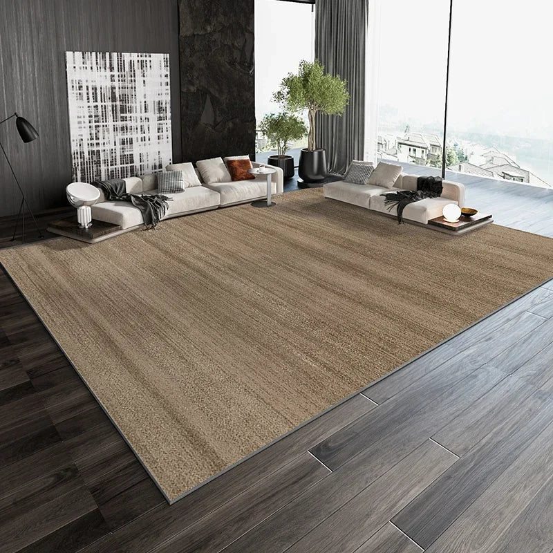 Un salon moderne avec un canapé et des coussins beiges, une grande fenêtre avec vue sur la nature, et un tapis beige qui couvre le sol en bois foncé.