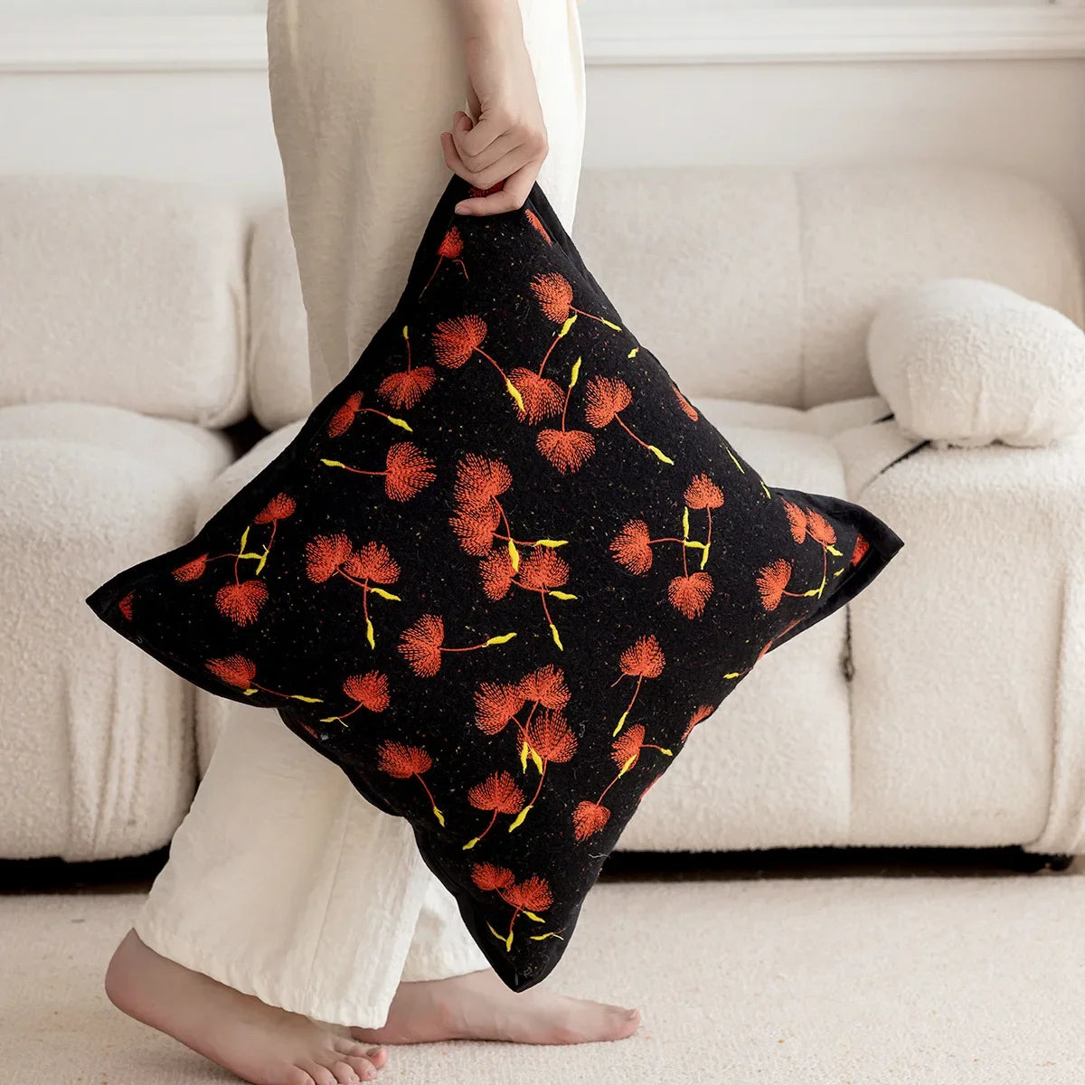 Un coussin décoratif noir avec des motifs de fleurs orange vives, créant une ambiance chaleureuse et élégante dans la pièce.