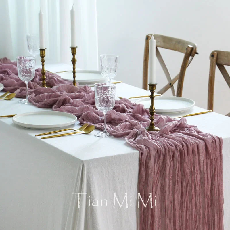 Une élégante table dressée avec des bougies, des verres cristallins et un magnifique chemin de table rose crêpé.