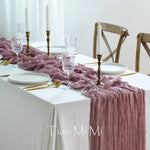 Une table de salle à manger élégamment dressée avec des chandelles, des verres en cristal et une nappe froissée dans des tons de rose et de blanc.