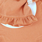 Une robe en tissu orange avec une jupe à volants et un nœud décoratif.