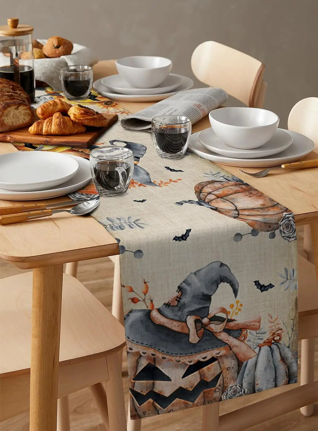 Sur une table en bois, un service à vaisselle élégant est disposé avec des croissants, des verres de vin et un chemin de table décoré de motifs d'Halloween.