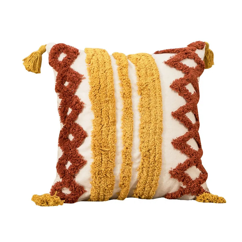 Coussin décoratif aux motifs graphiques en tons terracotta, jaune moutarde et crème, avec des pompons colorés.