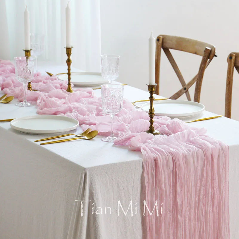 Une table élégante dressée avec de la vaisselle blanche, des chandeliers dorés et un chemin de table rose poudreux, créant une ambiance chaleureuse et raffinée.