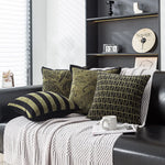 Coussins décoratifs en motif rayures et géométrique sur un canapé gris, entouré d'étagères avec des accessoires de décoration.