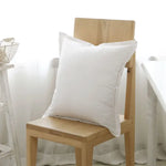 Coussin blanc confortable assis sur une chaise en bois dans un intérieur minimaliste.