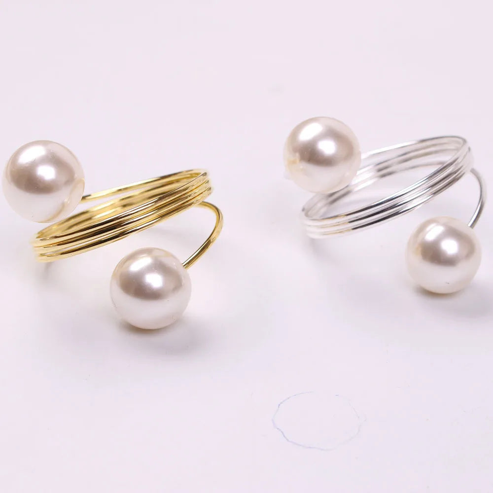 Des bagues de luxe en or et argent ornées de perles blanches brillantes, disposées avec élégance sur un fond uni.