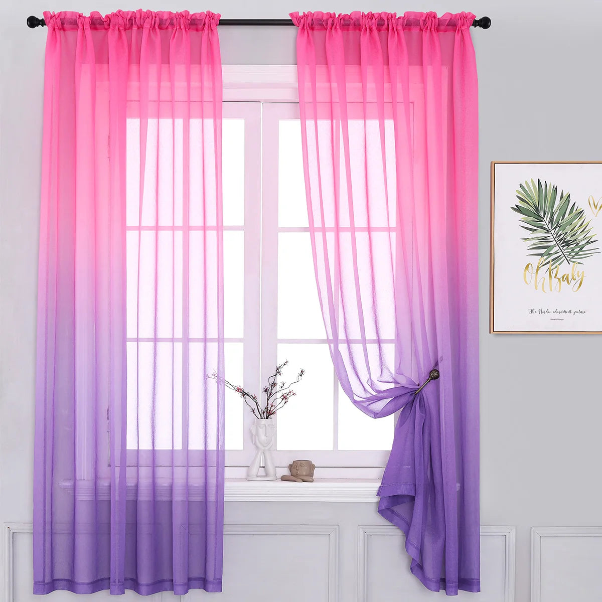 Voilage dégradé rose et violet encadrant une fenêtre dans un intérieur blanc avec tableau végétal encadré.