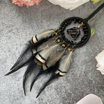 Boucle d'oreille artisanale avec un anneau noir et des plumes brun clair, décorée d'un élément en métal doré.