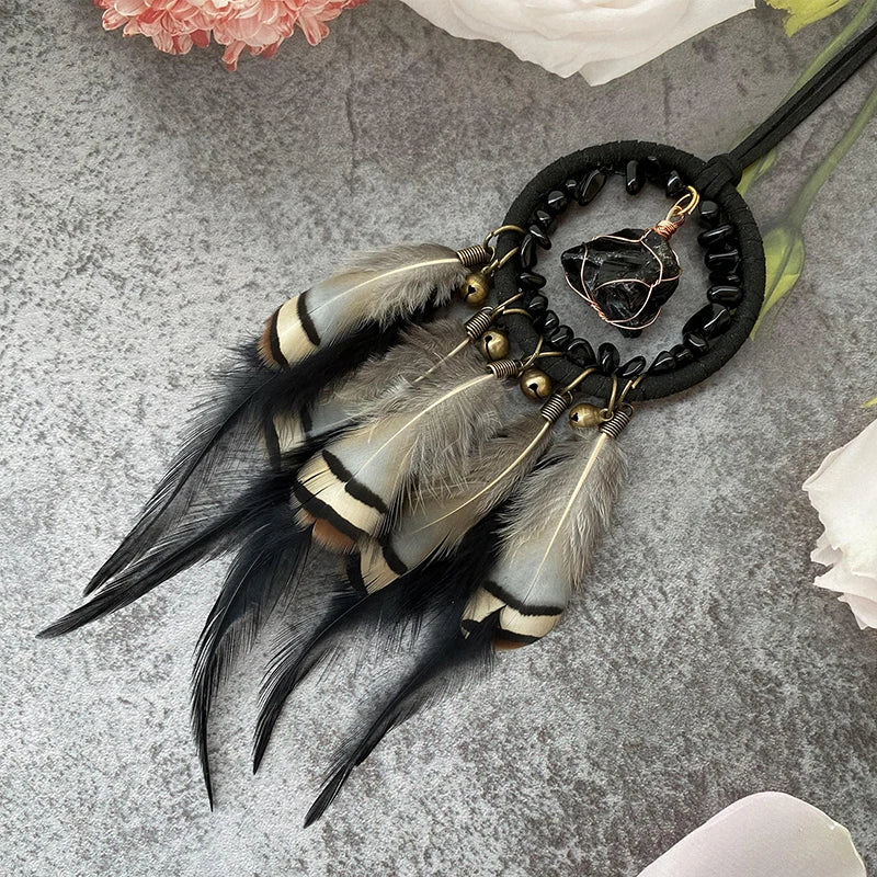 Boucle d'oreille artisanale avec un anneau noir et des plumes brun clair, décorée d'un élément en métal doré.