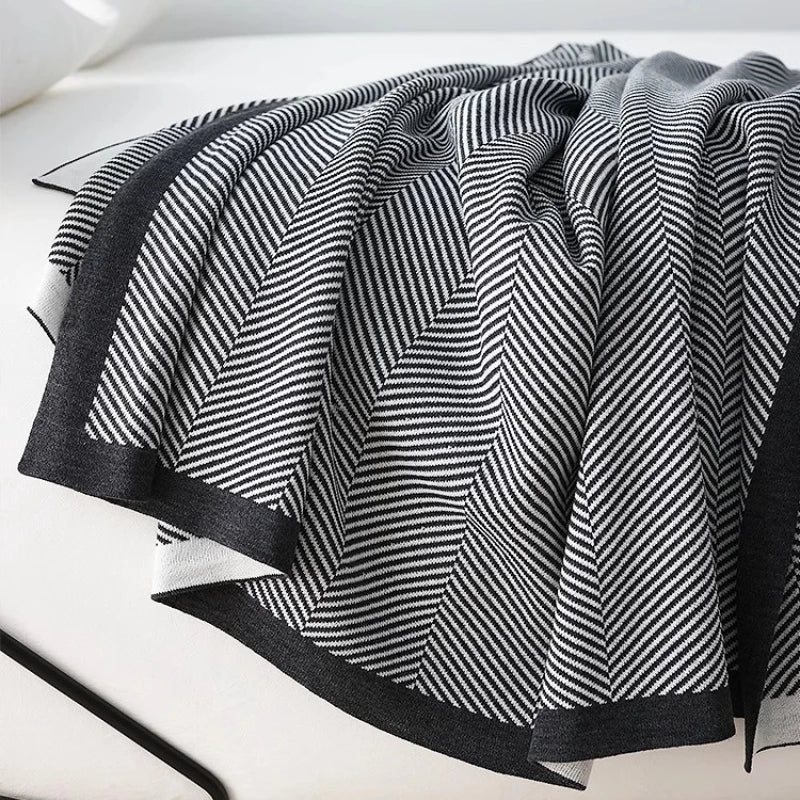 Couverture tricotée en noir et blanc avec un motif de lignes diagonales créant un effet ondulé et texturé, créant une impression élégante et sophistiquée.