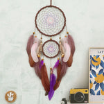 Une décoration murale originale en forme d'attrape-rêves avec des plumes multicolores et des perles dorées, créant une ambiance bohème chaleureuse.