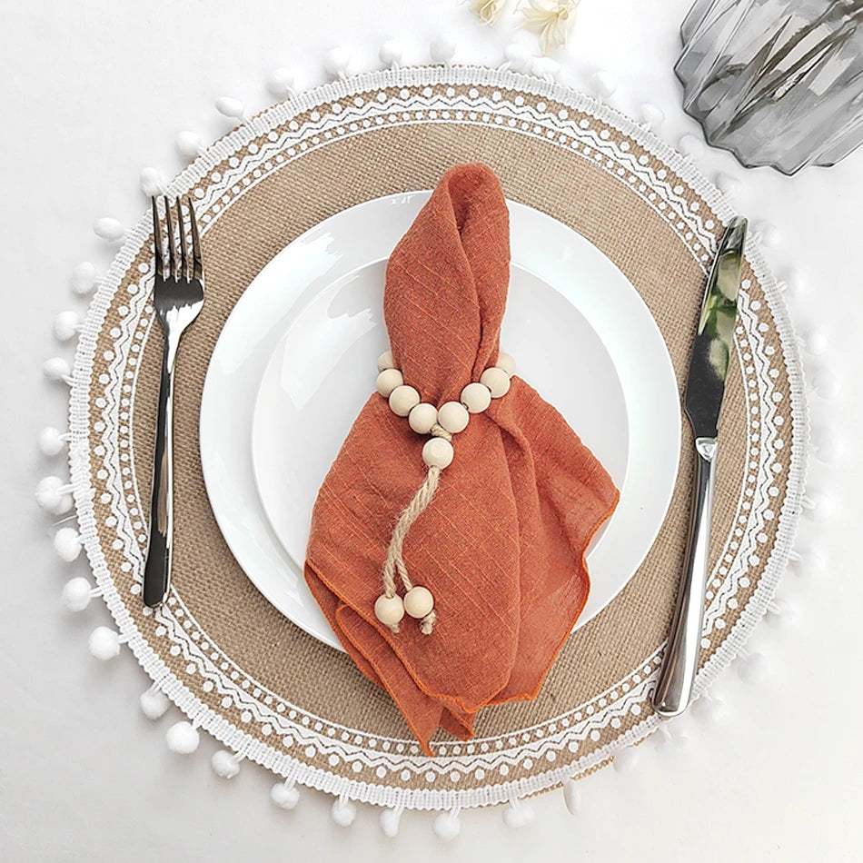 Élégante table de fête avec nappe texturée, assiette blanche, serviette en tissu orange et perles décoratives, créant une atmosphère chaleureuse et raffinée.