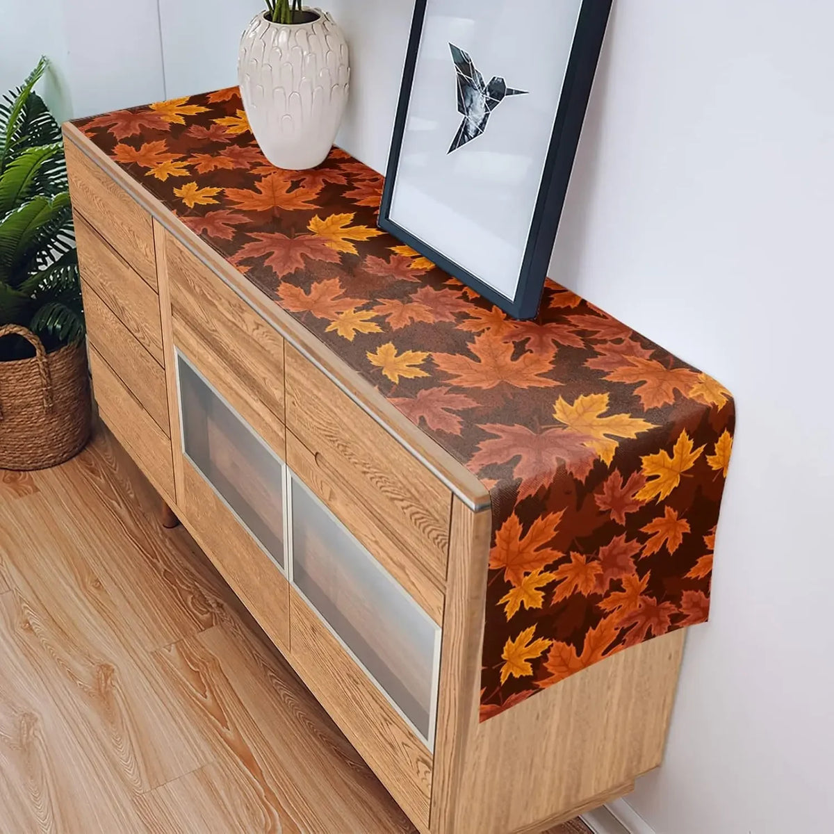 Buffet en bois avec un chemin de table décoré de feuilles d'automne colorées, accentuant l'ambiance chaleureuse et automnal de la pièce.