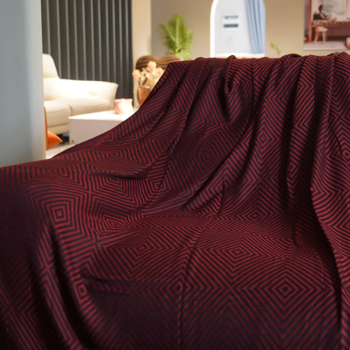 Cette image montre un plaid de couleur bordeaux décoré de motifs géométriques répétitifs en nuances de rouge, créant un effet élégant et sophistiqué dans un intérieur cosy.