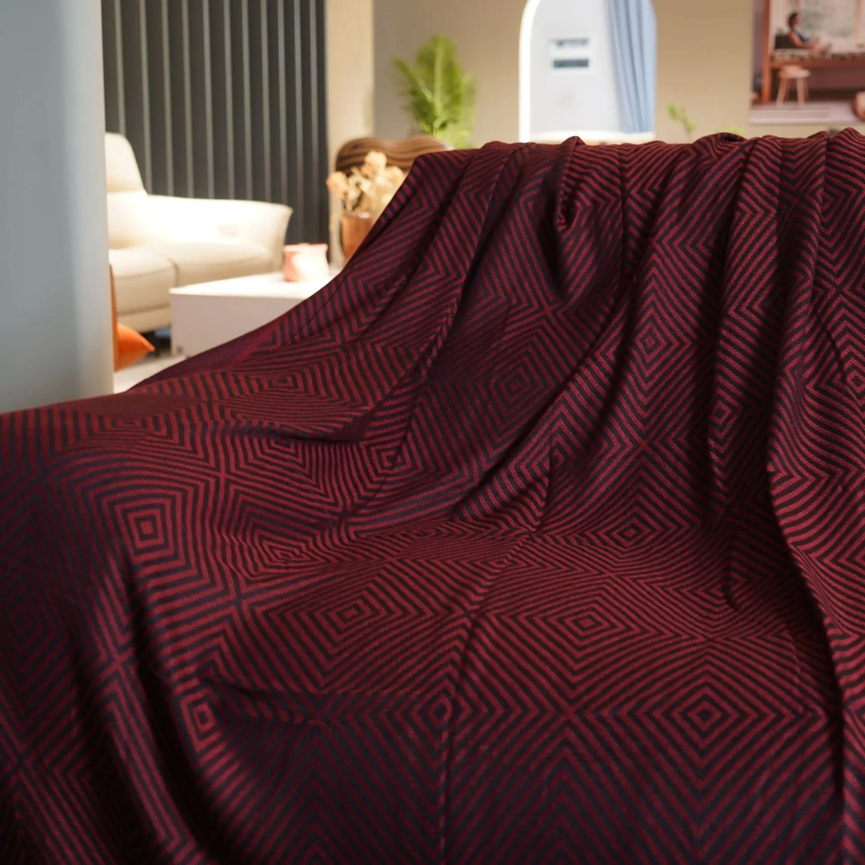 Cette image montre un plaid de couleur bordeaux décoré de motifs géométriques répétitifs en nuances de rouge, créant un effet élégant et sophistiqué dans un intérieur cosy.