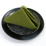 Serviette de table pliée en forme de triangle sur une assiette de céramique noire avec des paillettes.