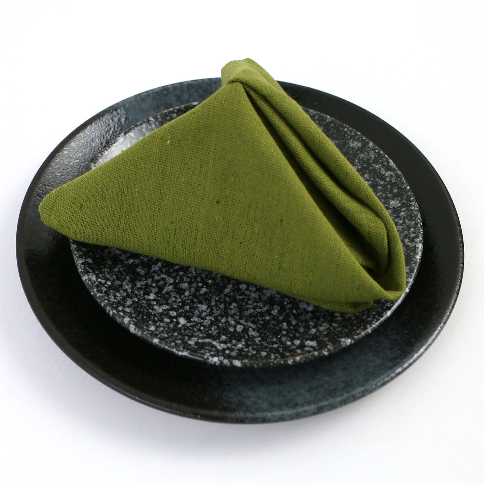 Serviette de table pliée en forme de triangle sur une assiette de céramique noire avec des paillettes.