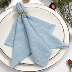 Serviette de table grise décorée de perles dorées, sur une assiette blanche avec un cadre doré et des accessoires floraux.