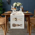 Table dressée avec fleurs blanches, verres à vin et décorations sur une nappe blanche à motifs.