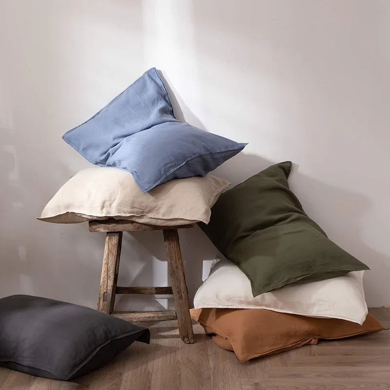 L'image montre un arrangement de coussins de couleurs neutres, notamment des coussins gris, beige et verts, posés sur un tabouret en bois, créant une ambiance confortable et cosy.