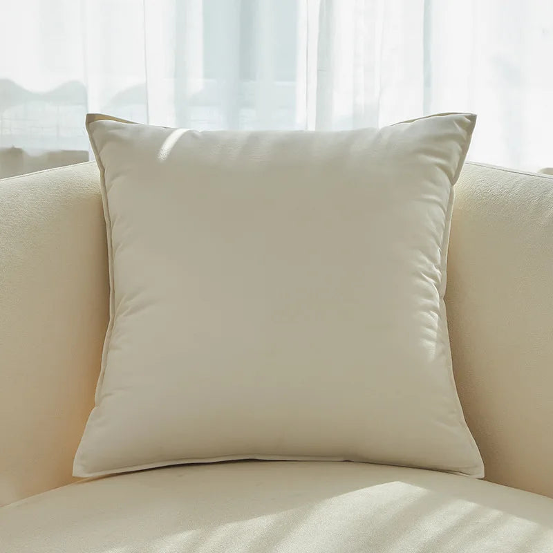 Coussin beige douillet posé sur un canapé clair près d'une fenêtre.