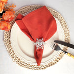 L'image montre une assiette blanche sur un tapis rond en fibres naturelles beiges, avec une serviette de table rouge ornée d'un motif de flocon de neige argenté, entourée de fleurs orange vives.