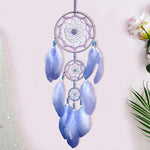 Un capteur de rêves décoratif et coloré, composé de plumes bleues et de cercles en corde, suspendu sur un fond clair avec des fleurs.