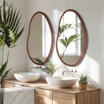 Le design minimaliste et élégant de cette salle de bain avec ses miroirs ovales en bois, ses lavabos blancs et son meuble en bois apporte une touche de nature grâce aux plantes vertes.