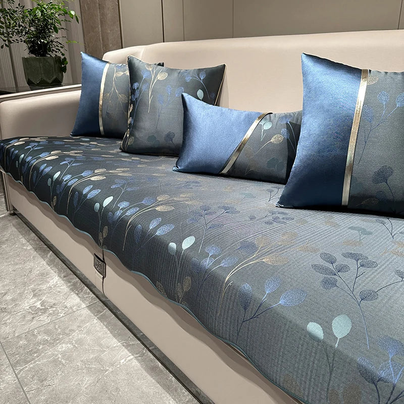 Un canapé gris avec des motifs bleus et argentés de feuilles et de branches, décoré de coussins assortis, créant une ambiance apaisante et naturelle dans un intérieur moderne.