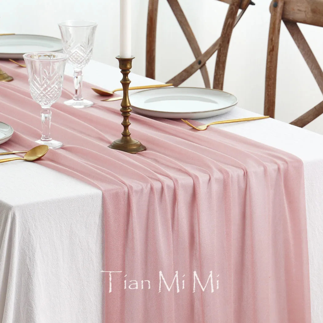Cette image présente une table élégante et raffinée, avec des assiettes, des verres et un chandelier en bronze sur une nappe rose pastel. L'ensemble crée une ambiance chaleureuse et conviviale, parfaite pour un dîner ou une réception.