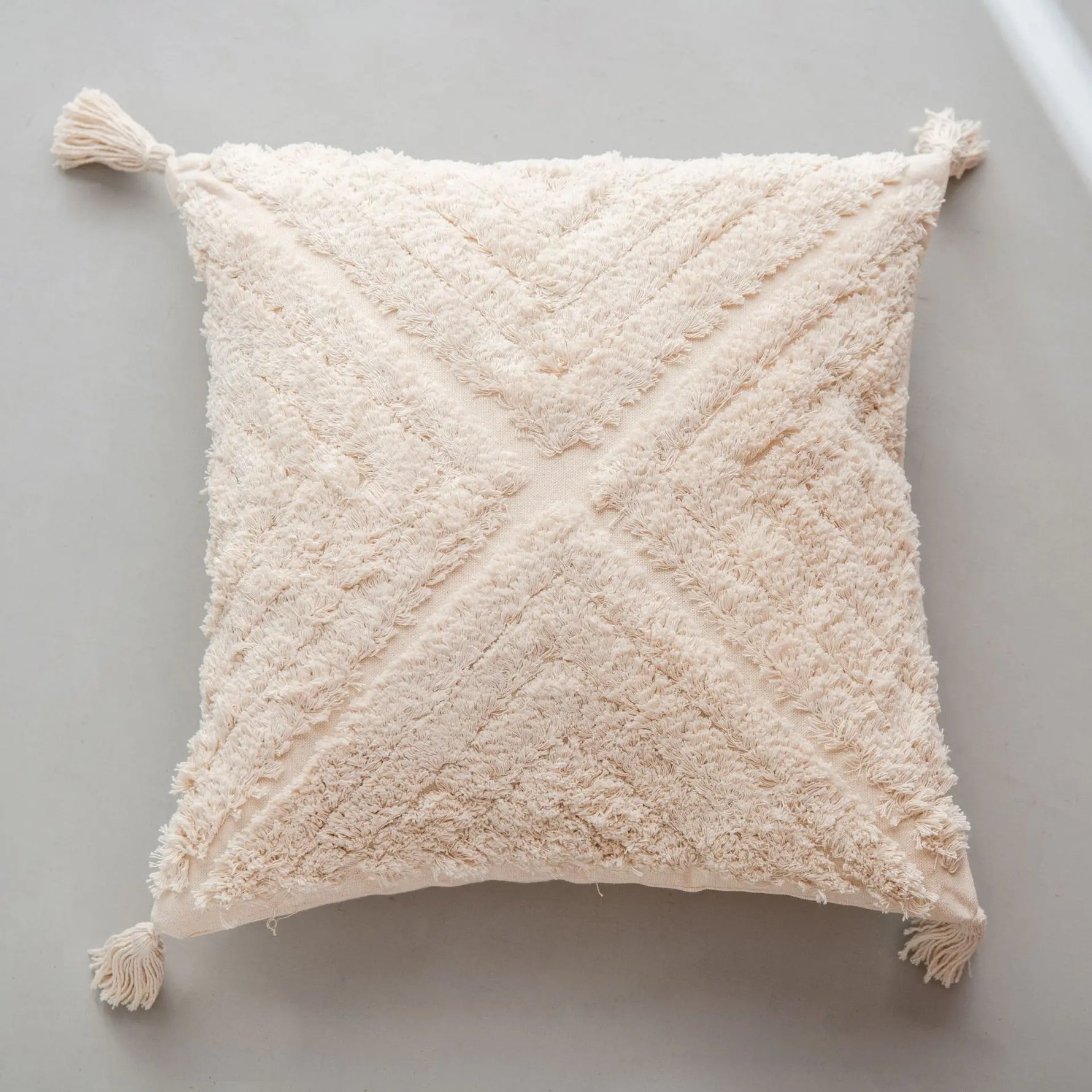 Coussin en tissu moelleux et pelucheux de couleur beige clair avec des motifs en diagonale et des glands aux coins.