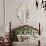 Cette image montre une chambre à coucher élégante avec un miroir ouvragé au-dessus d'une tête de lit en bois massif capitonnée de vert. La pièce est complétée par des accessoires de style vintage, comme une lampe de chevet en métal.