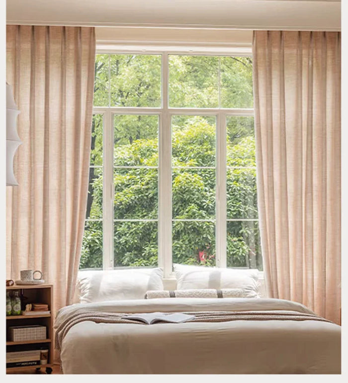 Voilage transparent marron clair en polyester dans une chambre lumineuse, encadrant une grande fenêtre donnant sur un jardin verdoyant.