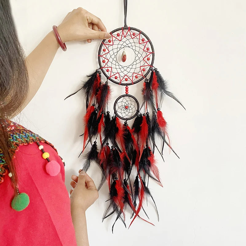 Attrapeur de rêves artisanal fait main avec motifs rouge et noir, plumes et perles, suspendu à une surface blanche.