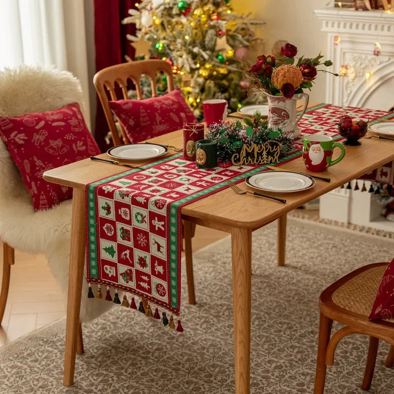 Table de salle à manger décorée pour Noël avec nappe ornée de motifs de Noël, décorations de fleurs et boules rouges, et beau sapin de Noël en arrière-plan illuminé.