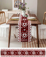 Table avec décoration romantique pour deux personnes, nappes rouges à motifs de cœurs, fleurs dans un vase, assiettes et verres sur une table en bois.