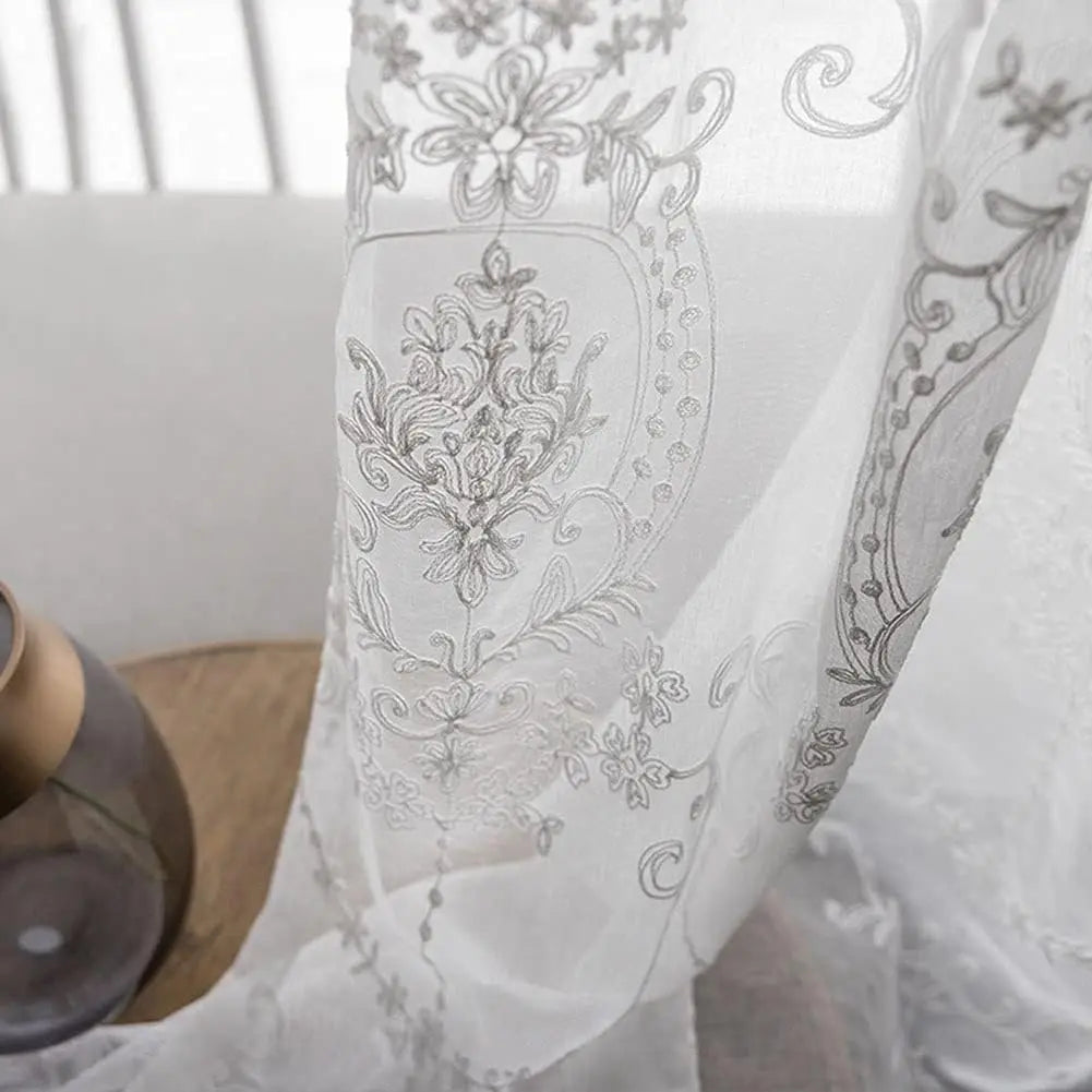 Détail raffiné des broderies délicates du voilage blanc, capturé sous la lumière du jour.
