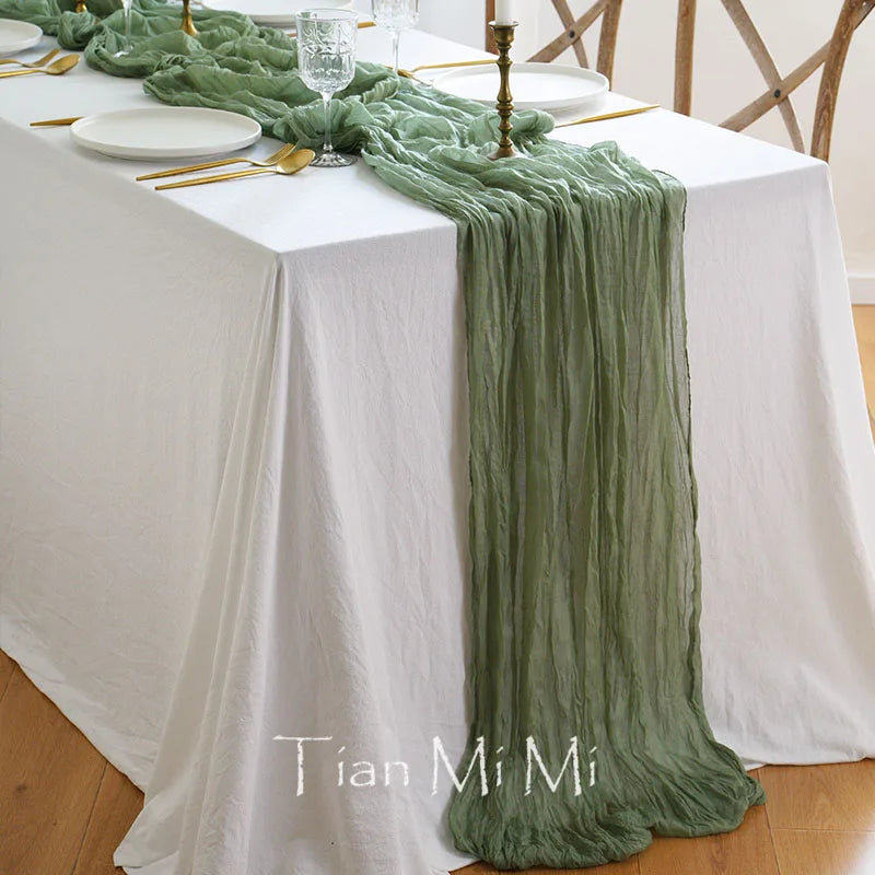 Cette image montre une table élégante avec un chemin de table en mousseline de soie vert clair, des assiettes blanches et des ustensiles dorés, suggérant un décor de salle à manger raffiné et harmonieux.