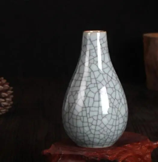 Vase décoratif en céramique craquelée blanche sur fond sombre avec un cône de pin.