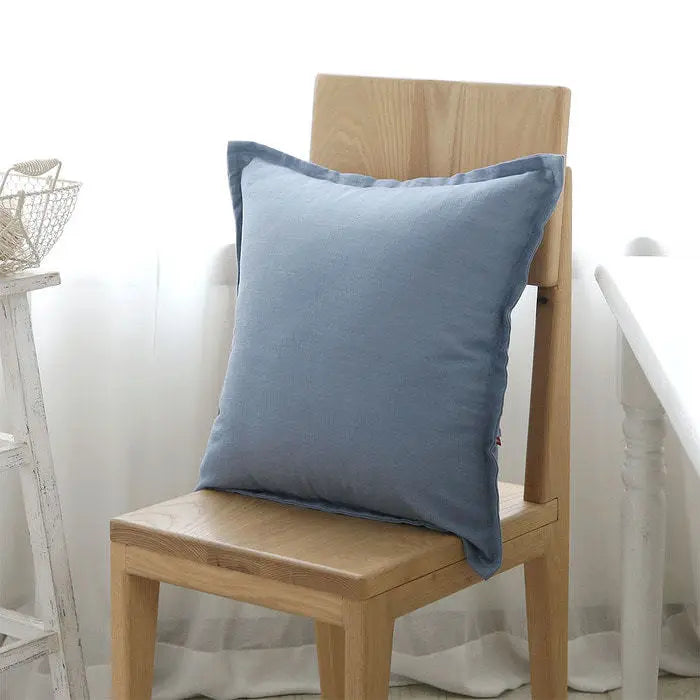 Coussin décoratif gris posé sur une chaise en bois clair, dans un intérieur lumineux et épuré.