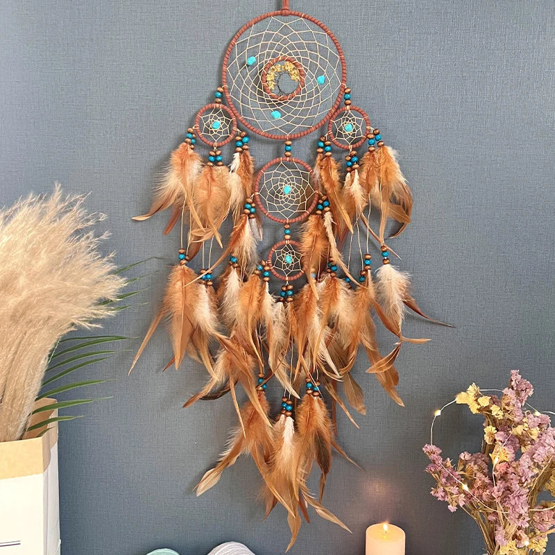 Attrapeur de rêves en macramé décoré de plumes et de perles turquoises, suspendu sur un mur gris.
